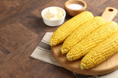 Photo of Tasty boiled corncobs, salt and butter on wooden table, closeup. Space for text