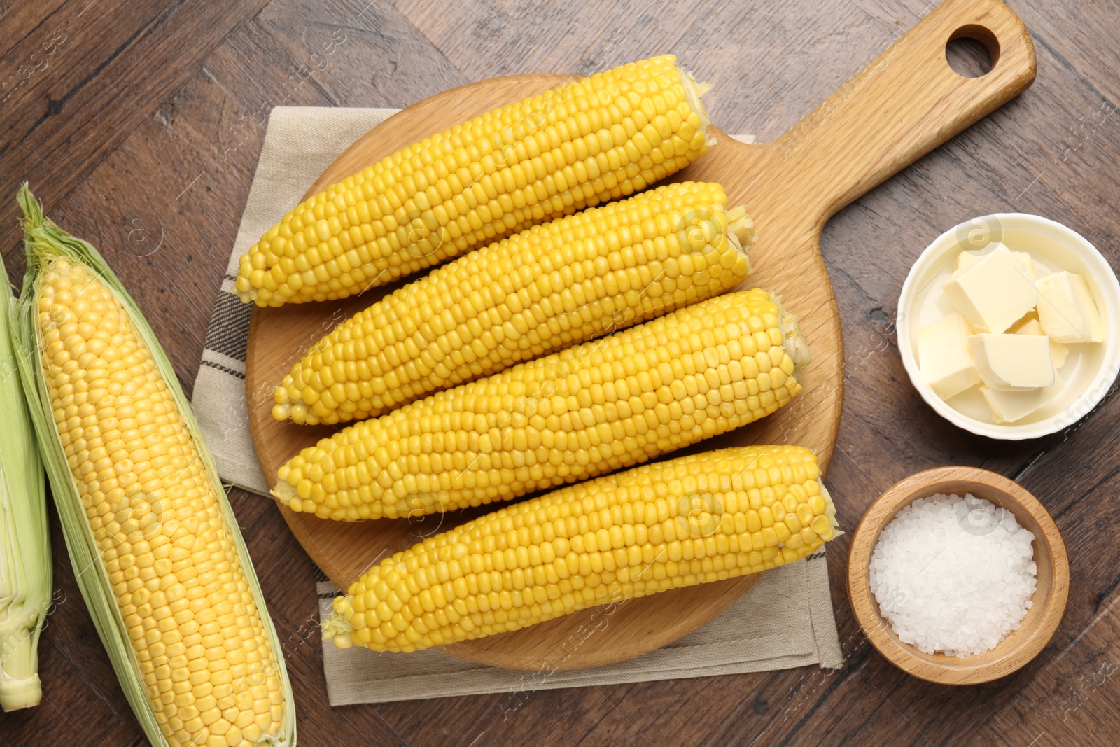 Tasty boiled corncobs, salt and butter on wooden table, flat lay Photo of Tasty boiled corncobs, salt and butter on wooden table, flat lay