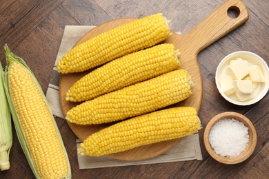Photo of Tasty boiled corncobs, salt and butter on wooden table, flat lay