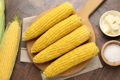 Photo of Tasty boiled corncobs, salt and butter on wooden table, flat lay