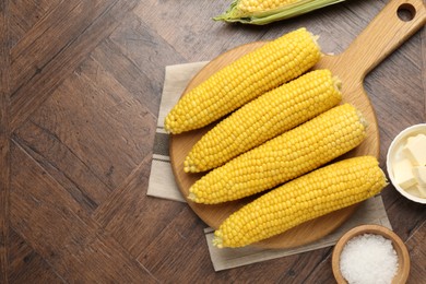 Photo of Tasty boiled corncobs, salt and butter on wooden table, flat lay. Space for text