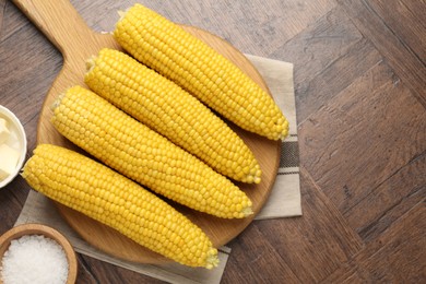 Photo of Tasty boiled corncobs, salt and butter on wooden table, flat lay