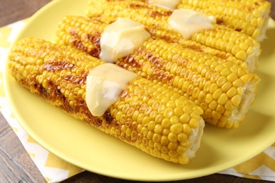 Photo of Tasty grilled corncobs with sauce on wooden table, closeup