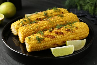 Photo of Tasty grilled corncobs with dill and lime slices on black table, closeup