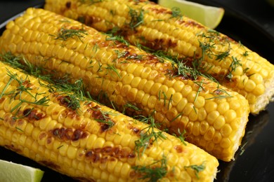 Photo of Tasty grilled corncobs with dill on black table, closeup