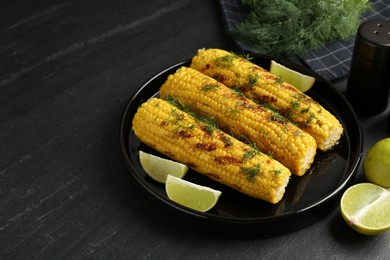 Photo of Tasty grilled corncobs with dill and lime slices on black table. Space for text