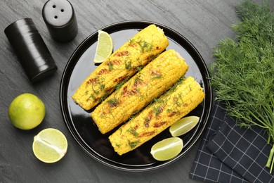 Photo of Tasty grilled corncobs with dill and lime slices on black table, flat lay