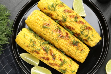 Photo of Tasty grilled corncobs with dill and lime slices on black table, flat lay