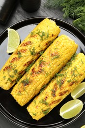 Photo of Tasty grilled corncobs with dill and lime slices on black table, flat lay