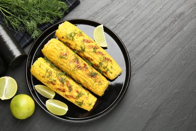 Photo of Tasty grilled corncobs with dill and lime slices on black table, flat lay