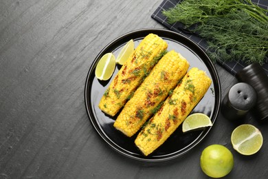 Photo of Tasty grilled corncobs with dill and lime slices on black table, flat lay
