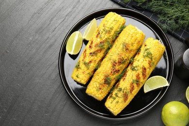 Photo of Tasty grilled corncobs with dill and lime slices on black table, flat lay