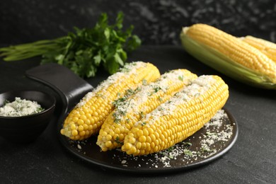 Photo of Tasty grilled corncobs with parsley and cheese on black table