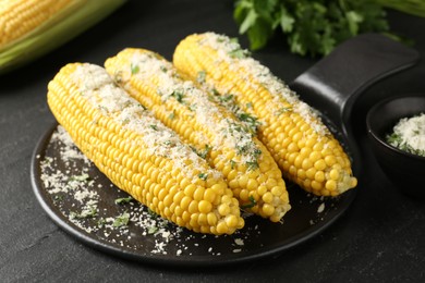 Photo of Tasty grilled corncobs with parsley and cheese on black table, closeup