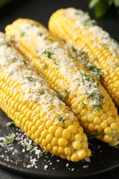 Photo of Tasty grilled corncobs with parsley and cheese on black table, closeup