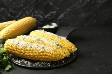 Photo of Tasty grilled corncobs with parsley and cheese on black table. Space for text