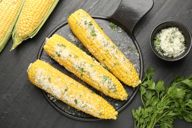 Photo of Tasty grilled corncobs with parsley and cheese on black table, flat lay