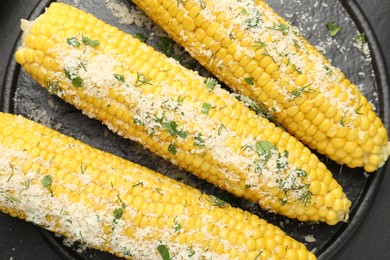 Photo of Tasty grilled corncobs with parsley and cheese on black table, top view
