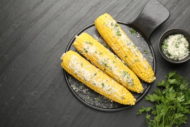 Photo of Tasty grilled corncobs with parsley and cheese on black table, flat lay