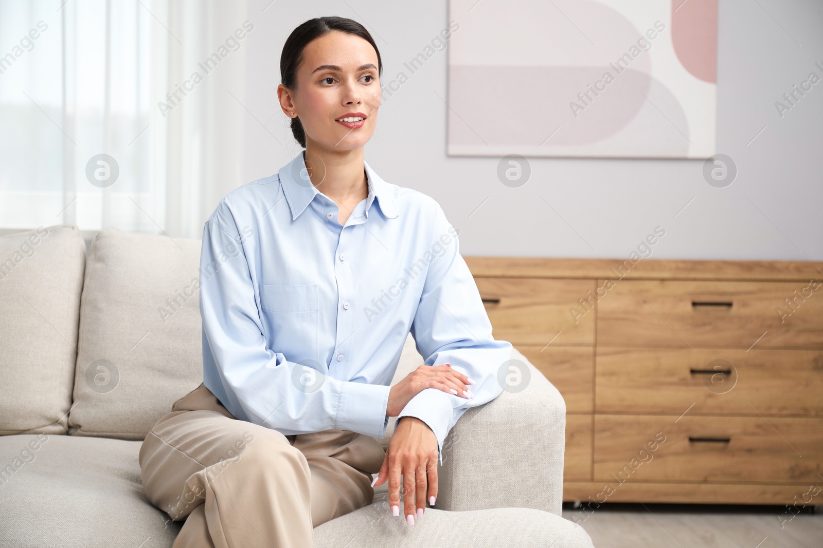 Photo of Elegant woman sitting on sofa at home. Space for text