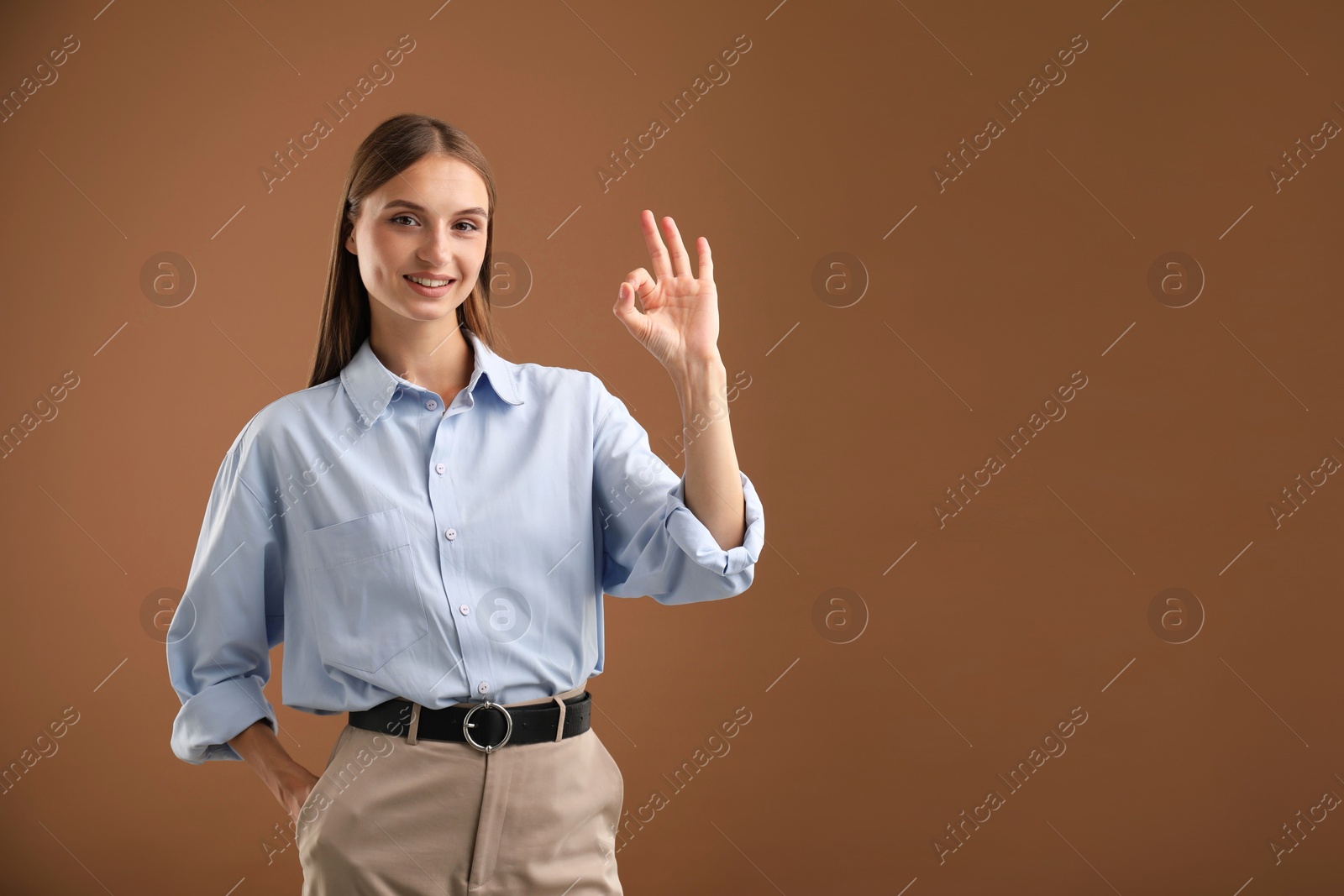 Photo of Beautiful woman showing okay gesture on brown background. Space for text
