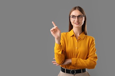 Photo of Confident woman pointing at something on grey background. Space for text