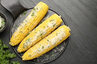 Photo of Tasty grilled corncobs with parsley and cheese on black table, flat lay