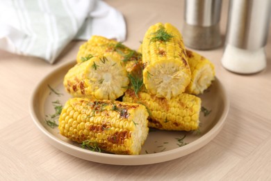 Photo of Pieces of tasty grilled corncobs with dill on wooden table, closeup