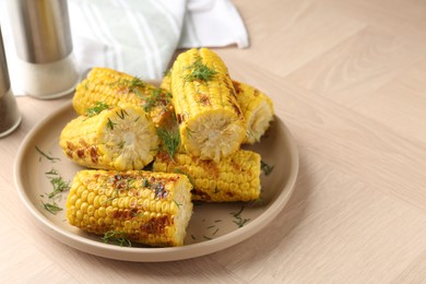 Photo of Pieces of tasty grilled corncobs with dill on wooden table, closeup