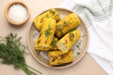 Photo of Pieces of tasty grilled corncobs with dill on wooden table, flat lay