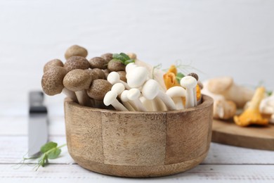 Photo of Different raw mushrooms and microgreens in bowl on light wooden table, closeup