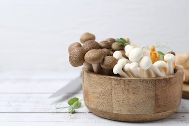 Photo of Different raw mushrooms and microgreens in bowl on light wooden table, closeup. Space for text