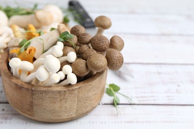 Photo of Different raw mushrooms and microgreens in bowl on light wooden table, closeup. Space for text
