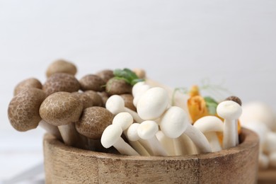 Photo of Different raw mushrooms in bowl on blurred light background, closeup
