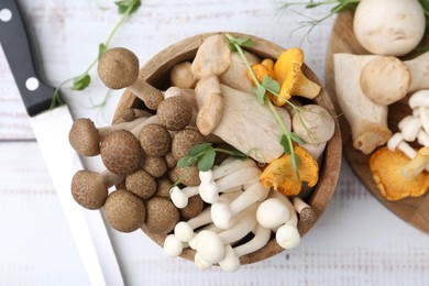 Photo of Different raw mushrooms, microgreens in bowl and knife on light wooden table, flat lay