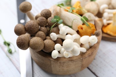 Photo of Different raw mushrooms and microgreens in bowl on light wooden table, closeup