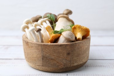 Photo of Different raw mushrooms and microgreens in bowl on light wooden table, closeup