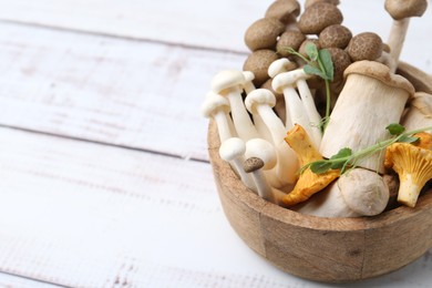 Photo of Different raw mushrooms and microgreens in bowl on light wooden table, closeup. Space for text