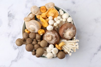 Photo of Different raw mushrooms in bowl on light marble table, top view