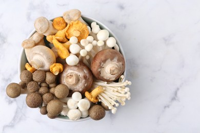 Photo of Different raw mushrooms in bowl on light marble table, top view. Space for text