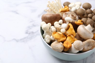 Photo of Different raw mushrooms in bowl on light marble table, closeup. Space for text