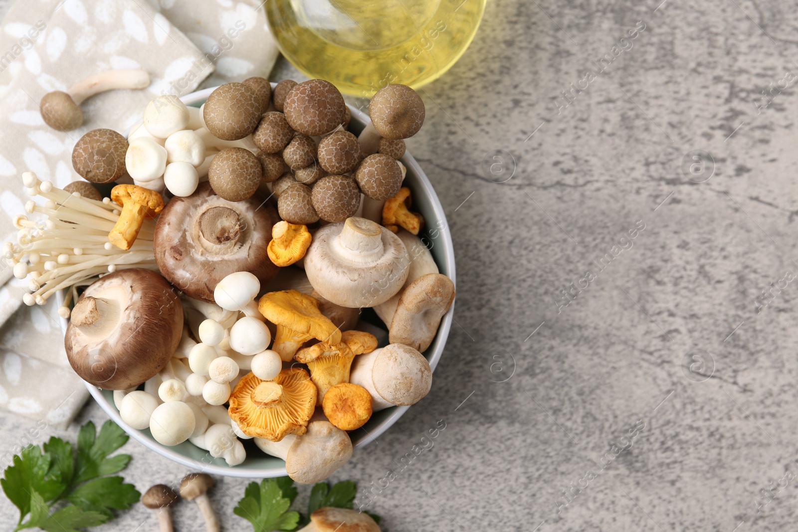 Different raw mushrooms in bowl, parsley and oil on grey textured table, flat lay. Space for text Photo of Different raw mushrooms in bowl, parsley and oil on grey textured table, flat lay. Space for text