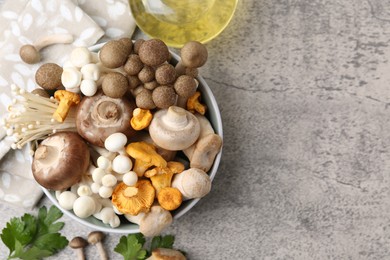 Photo of Different raw mushrooms in bowl, parsley and oil on grey textured table, flat lay. Space for text