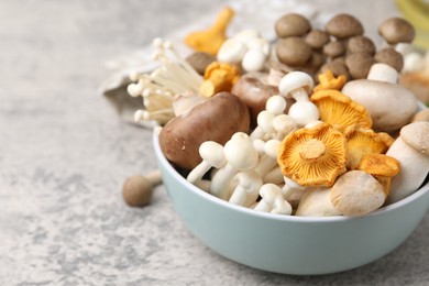 Photo of Different raw mushrooms in bowl on grey textured table, closeup. Space for text