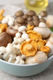 Photo of Different raw mushrooms in bowl on grey textured table, closeup