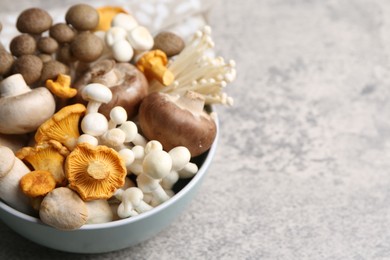 Photo of Different raw mushrooms in bowl on grey textured table, closeup. Space for text