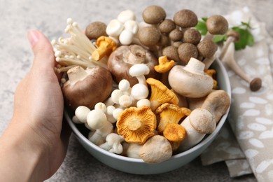 Photo of Woman with bowl of different raw mushrooms at grey textured table, closeup