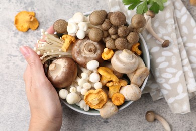 Photo of Woman with bowl of different raw mushrooms at grey textured table, top view