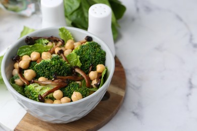 Photo of Delicious salad with shimeji mushrooms, chickpeas and broccoli in bowl on white marble table, closeup. Space for text