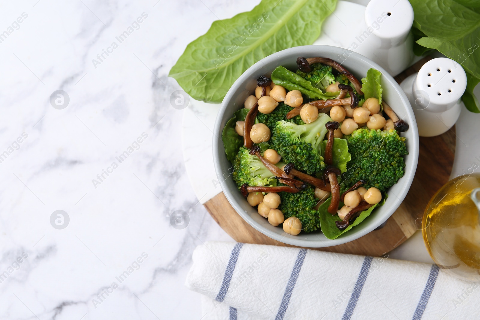 Photo of Delicious salad with shimeji mushrooms, chickpeas and broccoli in bowl on white marble table, flat lay. Space for text